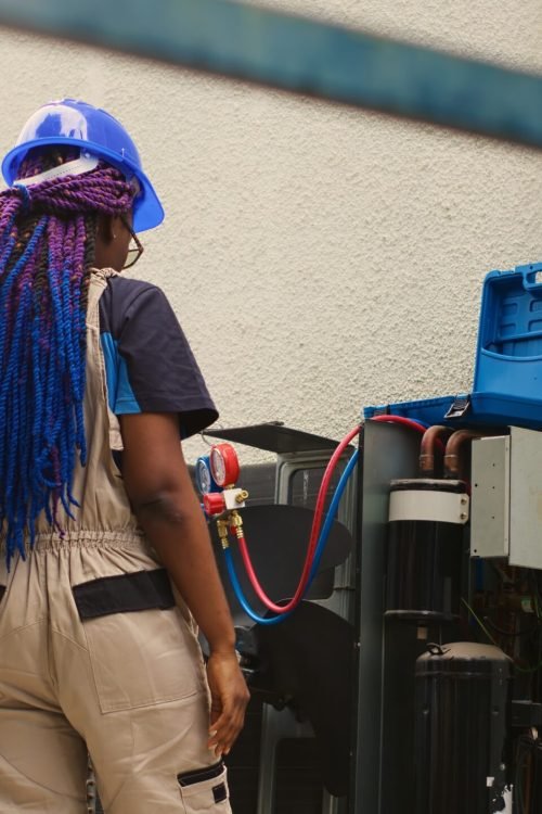 Diverse team of electricians brainstorming ways to repair out of order air conditioner while coworker steps down from folding ladder after finishing checking rooftop HVAC system